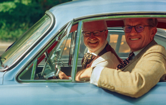 två leende män i en äldre bil